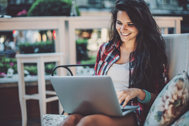 Happy young woman with laptop sitting on a couch outdoors, with copy space